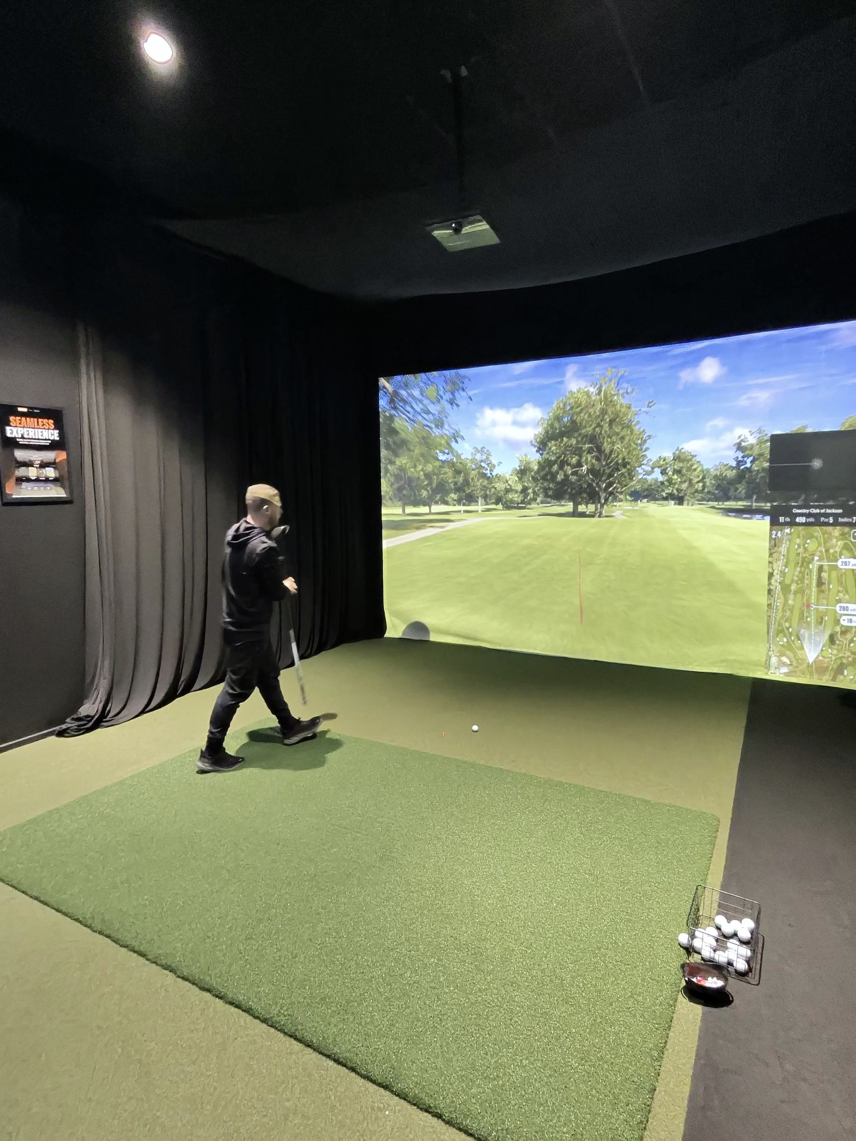 A golfer swinging inside a TOUR XP TrackMan simulator bay in Wigan